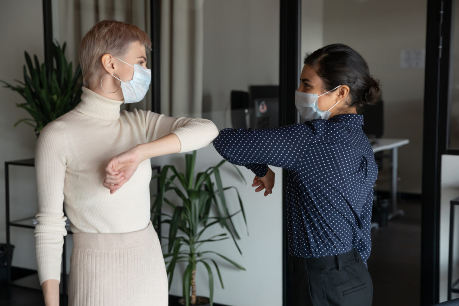 Two women bumping elbows with masks over their nose and mouth