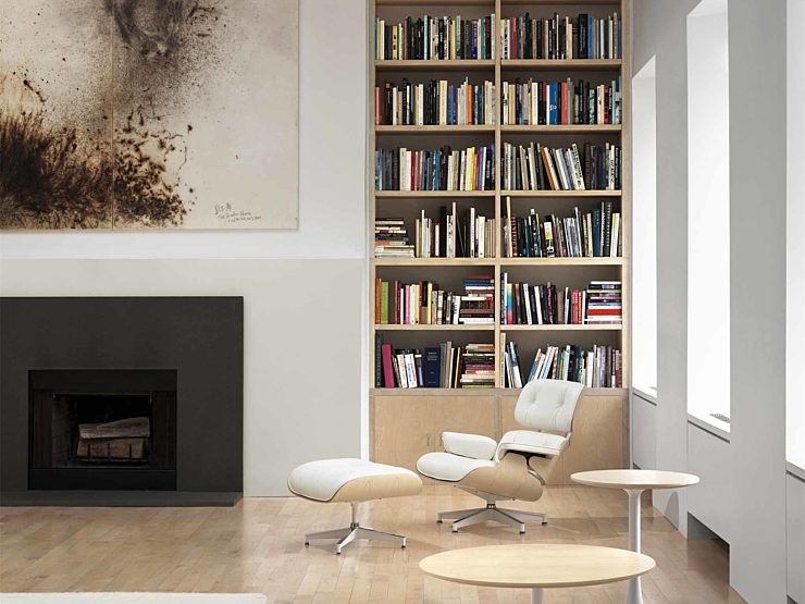 Eames Lounge chair in white leather in front of a fireplace and floor to ceiling bookshelf in a modern living room